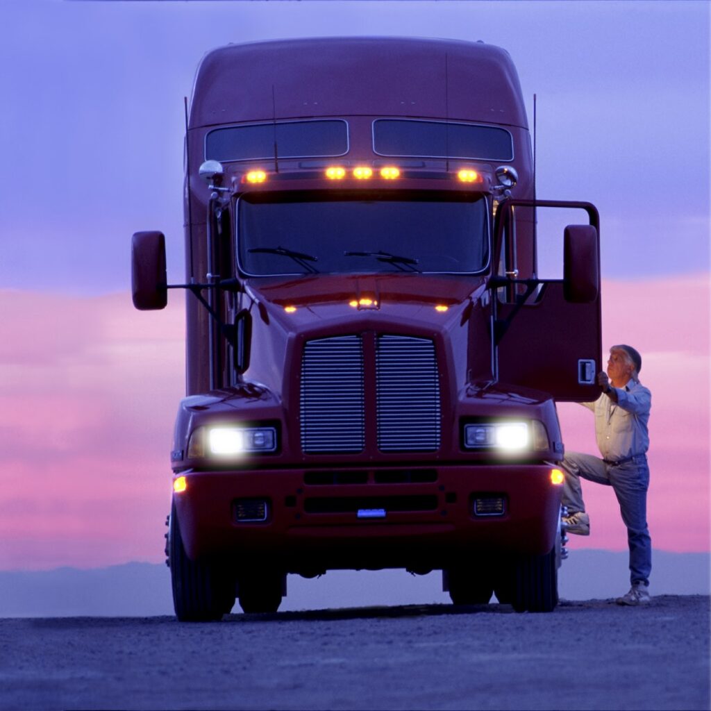 A silhouette of a truck driver getting into the cab of his commercial Class 8 truck tractor at